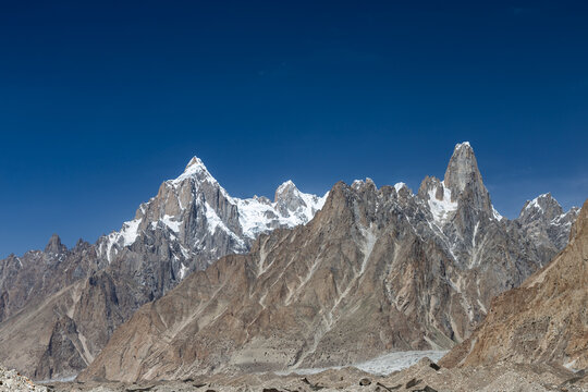 View of the majestic snow-capped peaks and rugged rocky slopes of the Baltoro Glacier under a clear blue sky in Baltoro, Gilgit Baltistan, Pakistan.