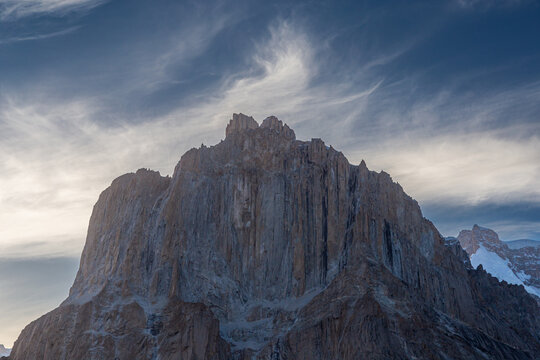 View of the dramatic, jagged rock spires of the Baltoro Glacier region, featuring sheer vertical cliffs and craggy peaks under wispy clouds, Baltoro, Gilgit Baltistan, Pakistan.