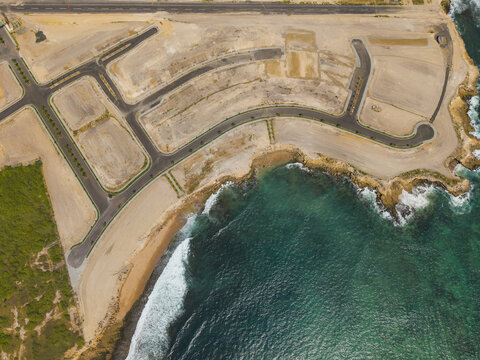 Aerial view of the coastal development site featuring paved roads, cleared land plots, and rocky cliffs meeting the turquoise Pacific Ocean waters in Ayangue, Santa Elena, Ecuador.