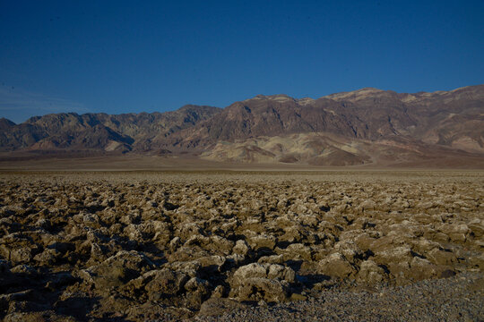 View of Devil's Golf Course with its jagged salt formations and distant mountains under a clear blue sky in Death Valley, California, United States.