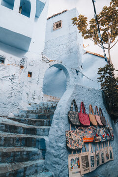 Chefchaouen, Morocco - 14 November 2025: View of blue-painted stone stairs and an archway in the historic medina of Chefchaouen, featuring colorful handmade tote bags on a wall.