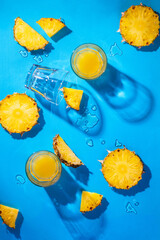 Pineapple pieces and pineapple juice isolated on blue background. Tropical holiday concept. Flat lay, top view © Nymphalyda