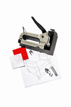 Silver furniture stapler gun with staples and the drawing of the armchair isolated on white background. Manual industrial tool