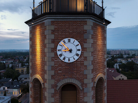 Aerial view of the illuminated clock tower of a historic brick church at twilight, overlooking the urban landscape of Krakow, Lesser Poland Voivode, Poland.