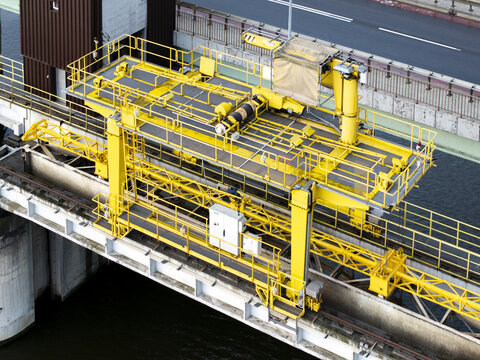 Aerial view of a yellow industrial gantry crane mechanism positioned on a bridge structure over a river in Krakow, Lesser Poland Voivode, Poland.