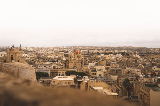 Valletta, Malta - 14 July 2022: View of the historic cityscape with traditional limestone buildings and a prominent church dome under a soft overcast sky.