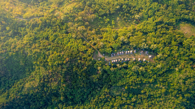 Aerial view of Kampung Adat Belaraghi nestled within the dense, lush green forests of the hills in Kecamatan Aimere, Nusa Tenggara Timur, Indonesia.