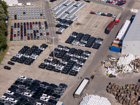 Aerial view of a large car storage lot filled with rows of new vehicles, trucks, and shipping pallets in Gdansk, Pomeranian Voivodeship, Poland.