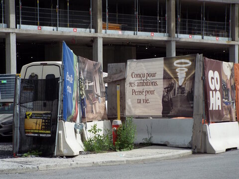 Gatineau, Quebec, Canada &ndash; June 16, 2026: A "construction site" features concrete barriers, temporary fencing, and banners with French text, with a building structure behind on Chem. Vanier.