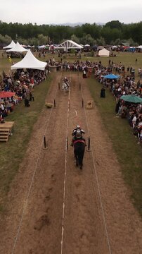 Loveland, United States - 09 June 2024: Aerial view of the Colorado Medieval Festival featuring knights in armor jousting in a dirt arena surrounded by spectators and white tents.