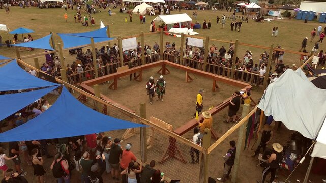 Loveland, United States - 09 June 2024: Aerial view of the Colorado Medieval Festival with knights in a wooden fighting ring surrounded by a large crowd under blue shade sails.