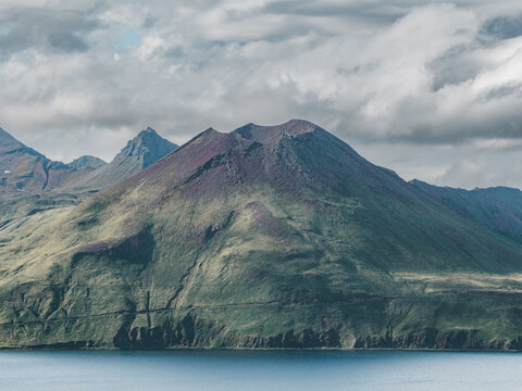 Aerial view of the volcanic landscape of Unalaska with green slopes and rocky peaks rising above the coastal waters in Unalaska, Alaska, United States.
