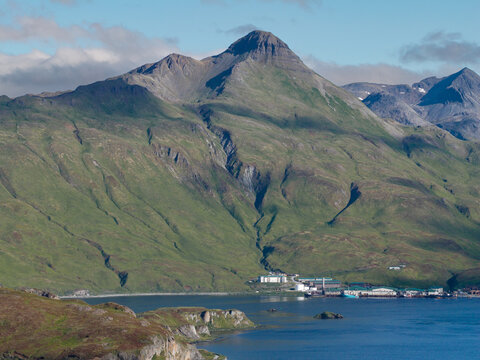 Aerial view of the rugged green mountains and coastal landscape of Unalaska with industrial buildings situated along the shoreline in Unalaska, Alaska, United States.