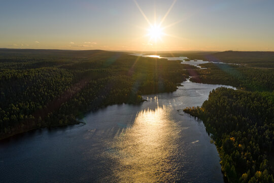 Aerial view of Perilajarvi lake surrounded by dense coniferous forests during a golden sunset in Enontekio, Lappi, Finland.