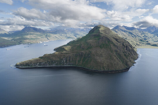 Aerial view of the rugged coastline and green hills of Unalaska island surrounded by the deep blue waters of the Bering Sea, Unalaska, Alaska, United States.