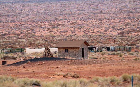 View of a stone cabin in the arid desert landscape of Monument Valley Tribal Park with horses in a corral and red earth in Oljato-Monument Valley, Utah, United States.