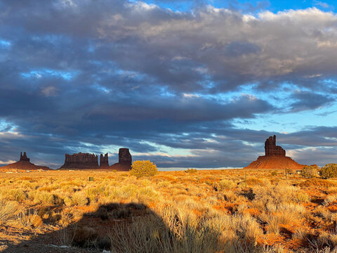 View of Monument Valley Tribal Park with iconic red sandstone buttes, desert scrub, and dramatic clouds at sunset in Oljato-Monument Valley, Utah, United States.