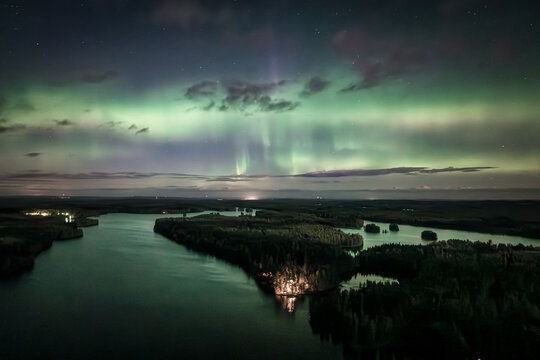 Aerial view of Laaminki lake illuminated by the vibrant green glow of the aurora borealis above dark forests and calm waters in Kangasniemi, Etela-Savo, Finland.