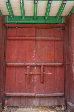 Red wooden double door with painted eaves on a traditional building in south korea.