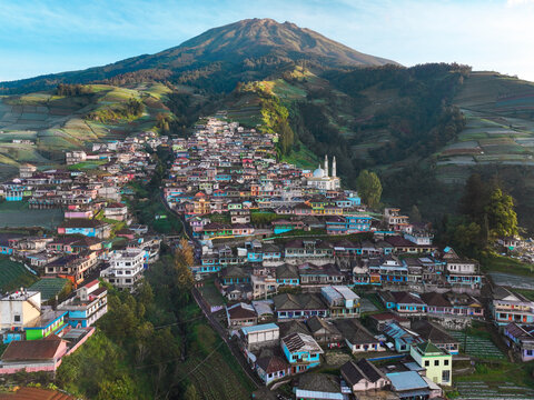 Aerial view of the colorful village nestled on the slopes of Mount Sumbing with terraced agricultural fields and a prominent mosque in Kaliangkrik, Central Java, Indonesia.