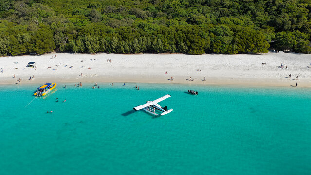 Aerial view of Whitehaven Beach with a seaplane anchored in turquoise water, white sand, lush forest, and people enjoying the beach in Whitsundays, Queensland, Australia.
