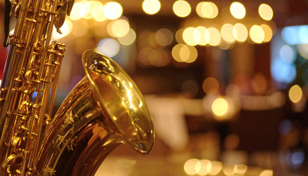 Saxophone musical instrument made of shiny brass standing in a dimly lit restaurant with beautiful golden blurred bokeh lights