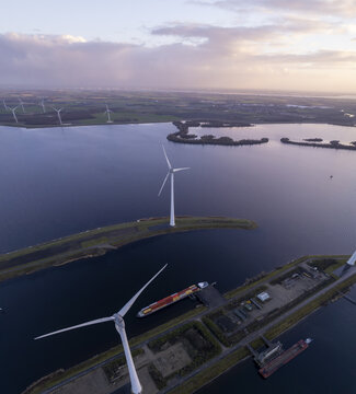 Aerial view of Krammer locks with wind turbines, a cargo ship in the waterway, and surrounding water and land at sunset in Bruinisse, Zeeland, Netherlands.