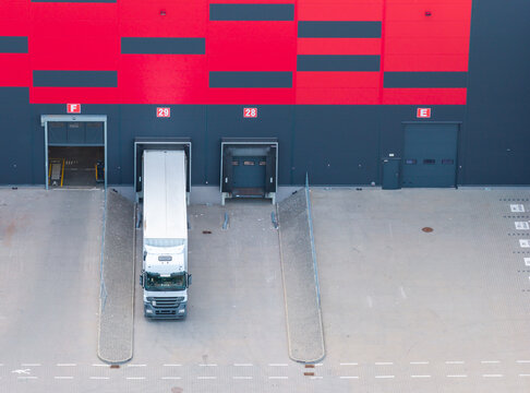 Aerial view of a logistics warehouse loading dock with a semi-truck parked at bay 29, featuring red and black exterior walls in Kowale, Pomeranian Voivodeship, Poland.