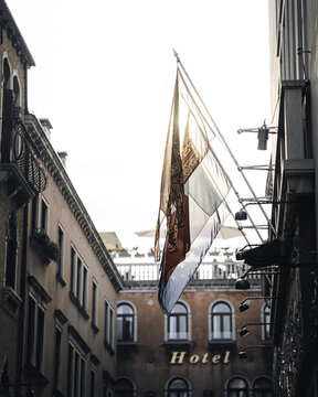 Venice, Veneto, Italy - 25 October 2024: View of a hotel building with hanging flags in a narrow street in Venice.