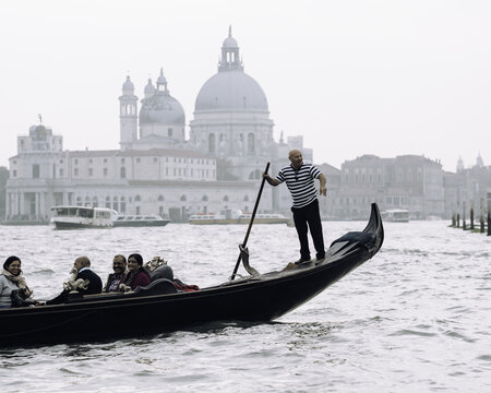 Venice, Italy - 25 October 2024: View of a gondolier steering a gondola with passengers on the Grand Canal with the Basilica di Santa Maria della Salute in the background.