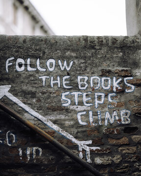 Venice, Veneto, Italy - 25 October 2024: View of a weathered brick wall featuring hand-painted white graffiti with the text 'FOLLOW THE BOOKS STEPS CLIMB' and a directional arrow.