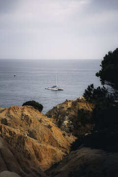 Faro District, Portugal - 20 September 2024: View of a catamaran sailing on the calm ocean waters framed by rugged orange cliffs and coastal vegetation in the Algarve region.