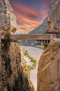 View of Caminito del Rey North Access with hikers on the narrow walkway suspended over the gorge and river below at sunset in Ardales, Andalucia, Spain.