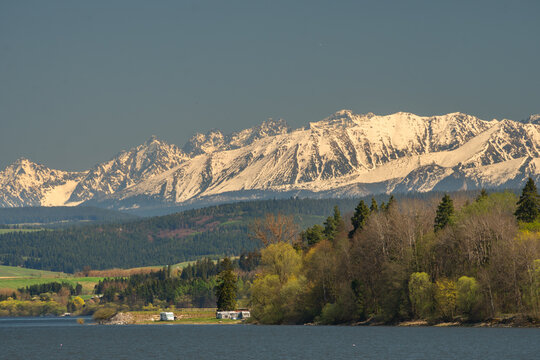 View of the Orava Reservoir and the snow-capped High Tatras mountains under a clear sky in Trstena, Zilina Region, Slovakia.
