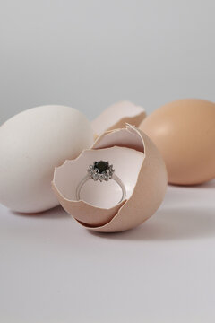 Elegant engagement ring with a black gemstone surrounded by whole eggs on a light background. Creative conceptual photography for a surprise proposal, hidden treasure, or new beginnings.