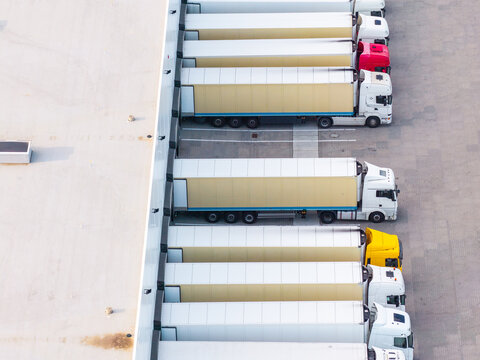 Aerial view of Gdansk-Kowale Distribution Centre with semi-trucks parked at loading docks, showing trailers, asphalt yard, and warehouse roof in Kowale, Pomeranian Voivodeship, Poland.