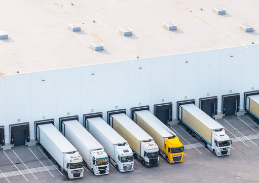 Aerial view of Gdansk-Kowale Distribution Centre with multiple semi-trucks parked at loading docks, showing white warehouse walls and asphalt yard in Kowale, Wojewodztwo pomorskie, Poland.