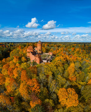 Aerial view of Turaida Castle surrounded by a vibrant autumn forest with colorful orange and yellow foliage under a clear blue sky in Sigulda, Sigulda Municipality, Latvia.