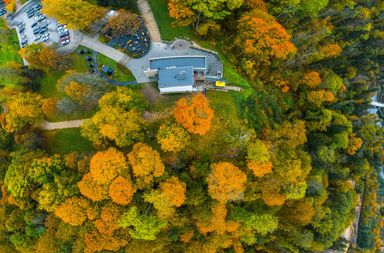 Aerial view of Sigulda park area with vibrant autumn foliage, a modern building, and a parking lot surrounded by dense trees in Sigulda, Sigulda Municipality, Latvia.