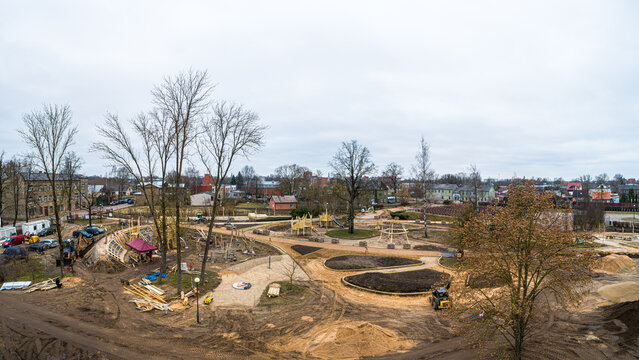 Aerial view of a park under construction with wooden playground structures, winding paths, and landscaping work in progress in Latvia.