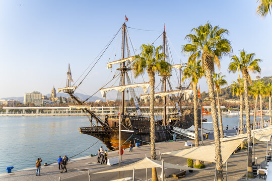 Malaga, Spain - 10 January 2020: View of a historic galleon replica docked at the Palmeral de Las Sorpresas in Malaga port, with palm trees and people walking along the promenade.