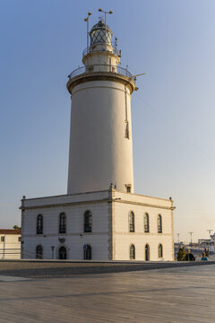 View of La Farola de Malaga lighthouse with its white tower and square base under a clear blue sky in Malaga, Andalusia, Spain.
