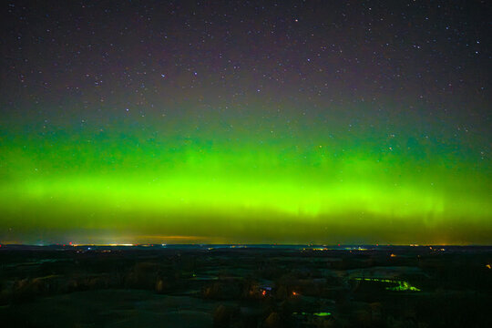 Aerial view of the vibrant green Aurora Borealis illuminating the night sky above a dark landscape, Latvia.