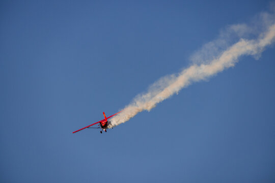 Druskininkai, Lithuania - 23 May 2026: View of a red stunt plane performing an aerobatic maneuver with a white smoke trail against a clear blue sky.