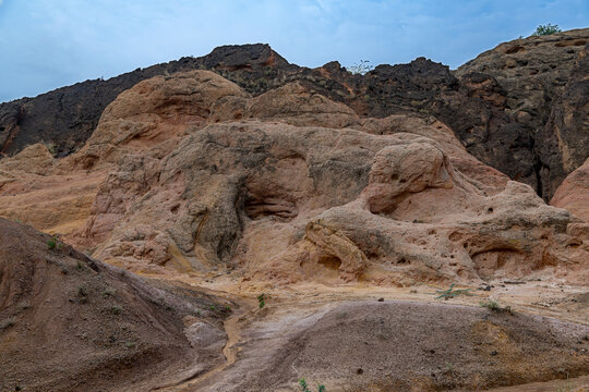 View of the rugged, colorful rock formations of the Sulaiman Mountains with deep red and brown soil under a cloudy sky in De-excluded Area Dera Ghazi Khan, Punjab, Pakistan.