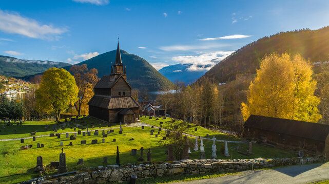 Aerial view of the historic wooden stave church surrounded by a cemetery with gravestones and vibrant autumn trees in Flam, Vestland, Norway.