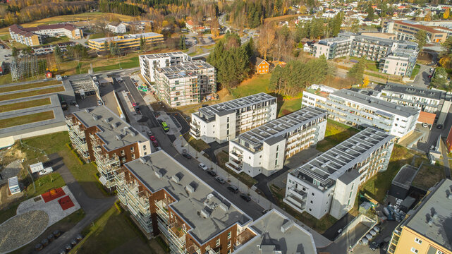 Aerial view of modern residential apartment buildings with flat roofs and parking areas surrounded by trees and autumn foliage in Sweden.