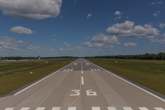 Aerial view of an airport runway with markings and green fields under a blue sky in Latvia.