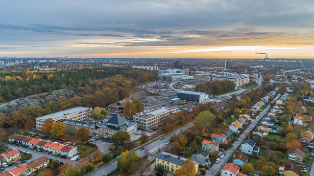 Aerial view of a suburban landscape featuring residential houses, autumn trees, and a construction site under a sunset sky, Sweden.