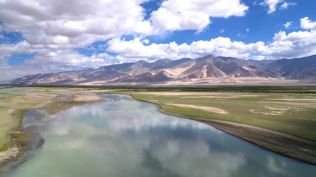 Aerial view of the Indus River flowing through the rugged landscape of Dungti with mountains and reflective clouds in the sky in Dungti, Ladakh, India.